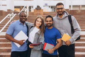 Diverse Group of Happy University Students Posing Together on Campus Steps Holding Notebooks A diverse group of university students smiling and standing on campus steps, holding notebooks and showing friendship and academic enthusiasm.